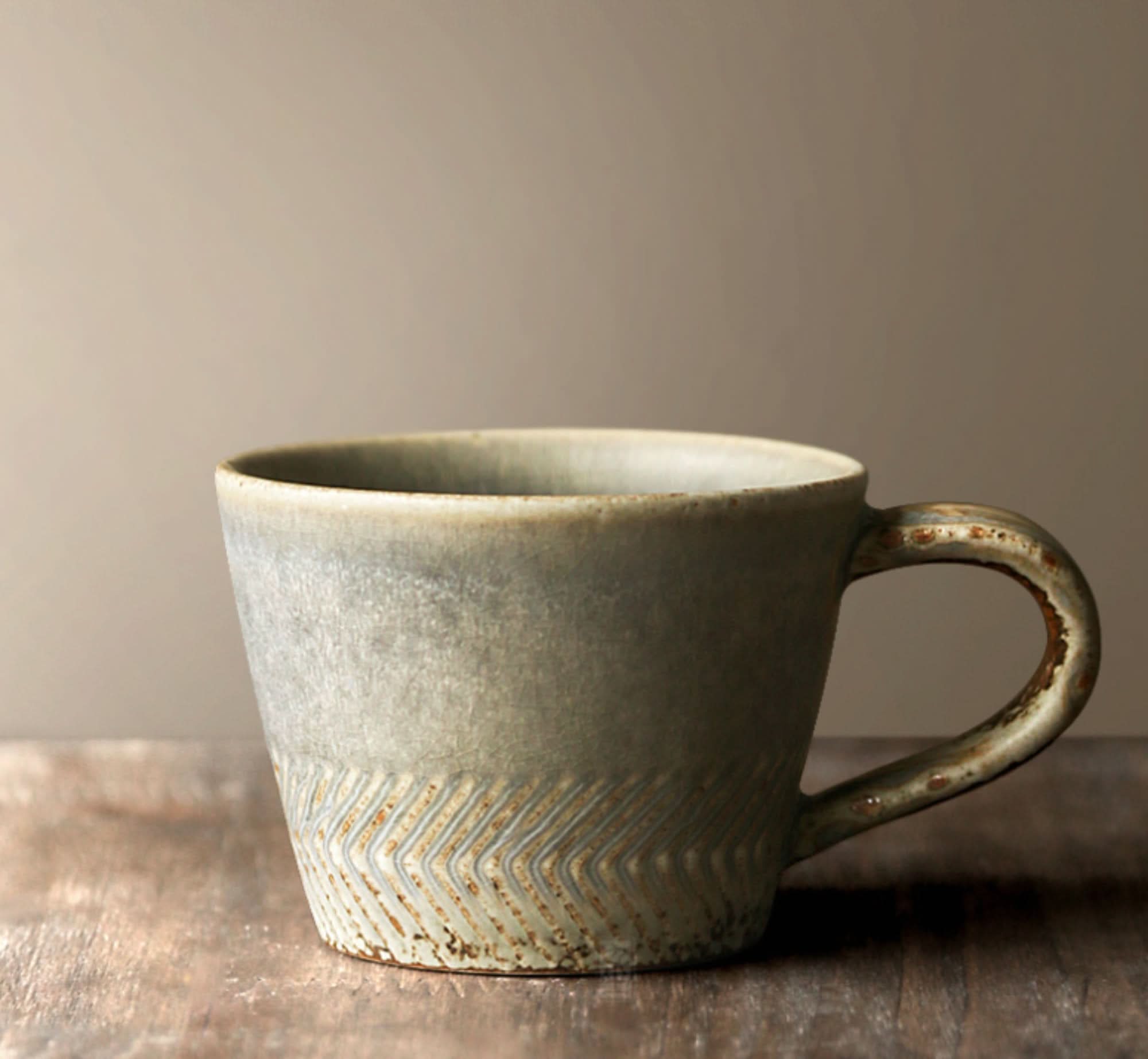 Gray stoneware Japanese Pottery Mug with carved texture on a rustic wooden surface.